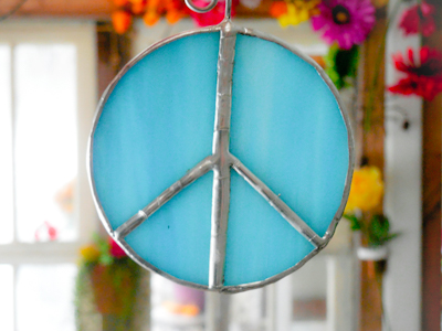 Aqua blue stained glass peace sign suncatcher with flowers in the background