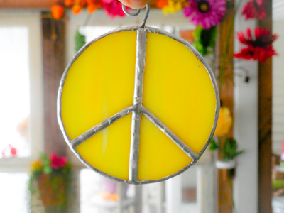 Yellow stained glass peace sign suncatcher with flowers in the background