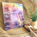 Designer Glass Iridized Amethyst Stained Glass sheet in front of jute background with plant for comparison showing rainbowy iridizing on a pinky type purple and white glass in the Mountain Woman Products studio