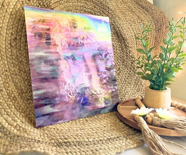 Designer Glass Iridized Amethyst Stained Glass sheet in front of jute background with plant for comparison showing rainbowy iridizing on a pinky type purple and white glass in the Mountain Woman Products studio