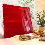 Oceanside Red & White Opal stained glass sheet with streaks of bright red and white next to a plant with daisies and beads in the Mountain Woman Products studio