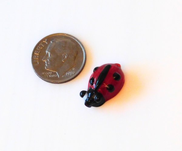 miniature lampwork glass ladybug bead next to a dime for comparison Mountain Woman Products