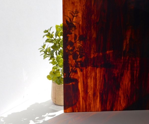 DG1068 Amber Chocolate Streaky Stained Glass Sheet with plant behind it showing opacity Mountain Woman Products