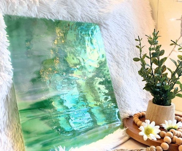 Designer Glass DG1075 Iridized Green & White stained glass sheet with a silvery color iridizing with a plant in front in Mountain Woman Products Studio