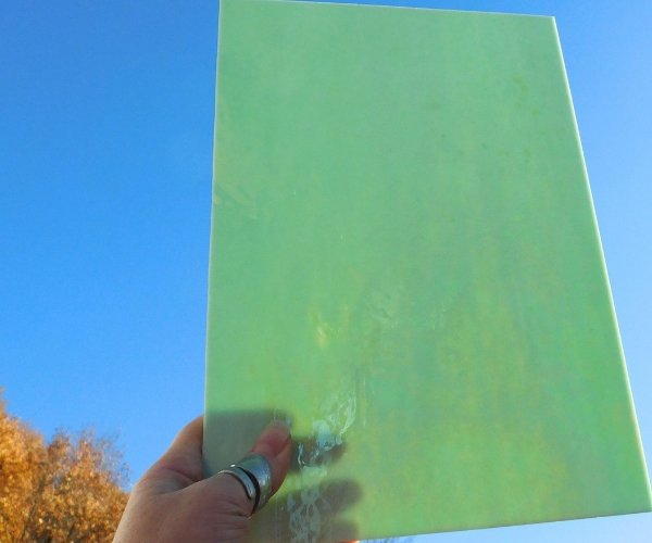Wissmach Pale Green Luminescent Iridized Fusible Stained Glass Sheet in the sun with hand holding it Mountain Woman Products