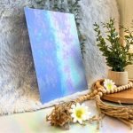 Wissmach Superior Blue Luminescent stained glass sheet with iridescent pink and aqua colors on it and a plant in the background of Mountain Woman Products studio