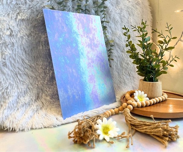 Wissmach Superior Blue Luminescent stained glass sheet with iridescent pink and aqua colors on it and a plant in the background of Mountain Woman Products studio