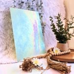 Wissmach Light Green Luminescent fusible glass sheet in a minty green with pink, yellow and aqua iridescence and a plant in the background at Mountain Woman Products studio