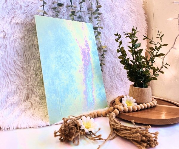 Wissmach Light Green Luminescent fusible glass sheet in a minty green with pink, yellow and aqua iridescence and a plant in the background at Mountain Woman Products studio