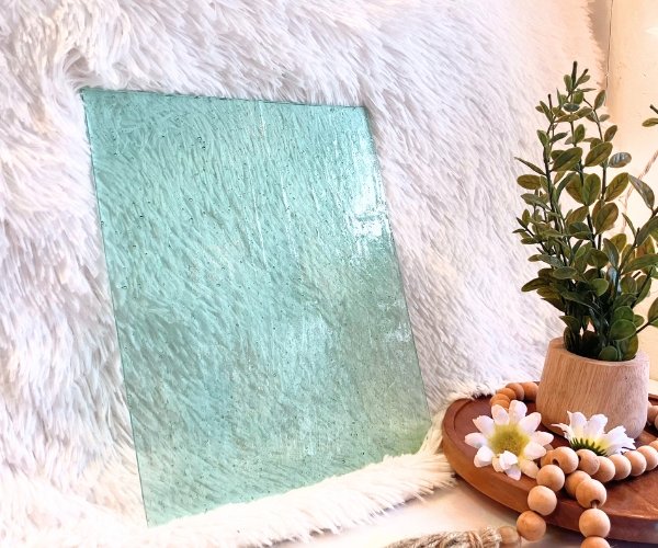 Wissmach Pale Green Seedy Stained Glass Sheet with a white background and a plant with daisies in the Mountain Woman Products studio