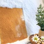 Wissmach Amber Seedy Stained Glass Sheet with a white background and a plant with daisies in the Mountain Woman Products studio