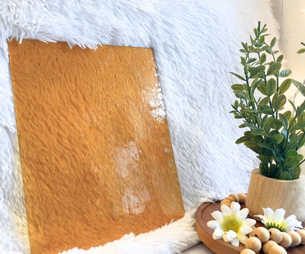 Wissmach Amber Seedy Stained Glass Sheet with a white background and a plant with daisies in the Mountain Woman Products studio