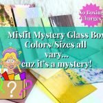 Misfit Mystery Glass Box with a variety of random stained glass pieces pictured are yellow purple green white iridescent rose and a fracture aqua and blue glass with the Mountain Woman Products logo girl holding a box of glass with a question marks on it