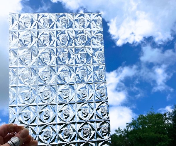 Kokomo KOG33WS Rosebud clear stained glass sheet with repeating rosebud raised patterns with a hand holding it to the blue sky with clouds Mountain Woman Products Studio