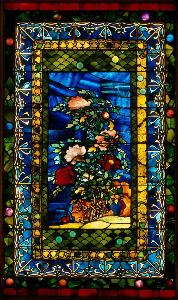John Lafarge Peonies Blown In The Wind c.1880 Stained Glass Window with every color including peach, coral and red peonies bloomed and a deep blue sky with a peony bud border with red pink blue and deep orange Photo courtesy Met Museum
