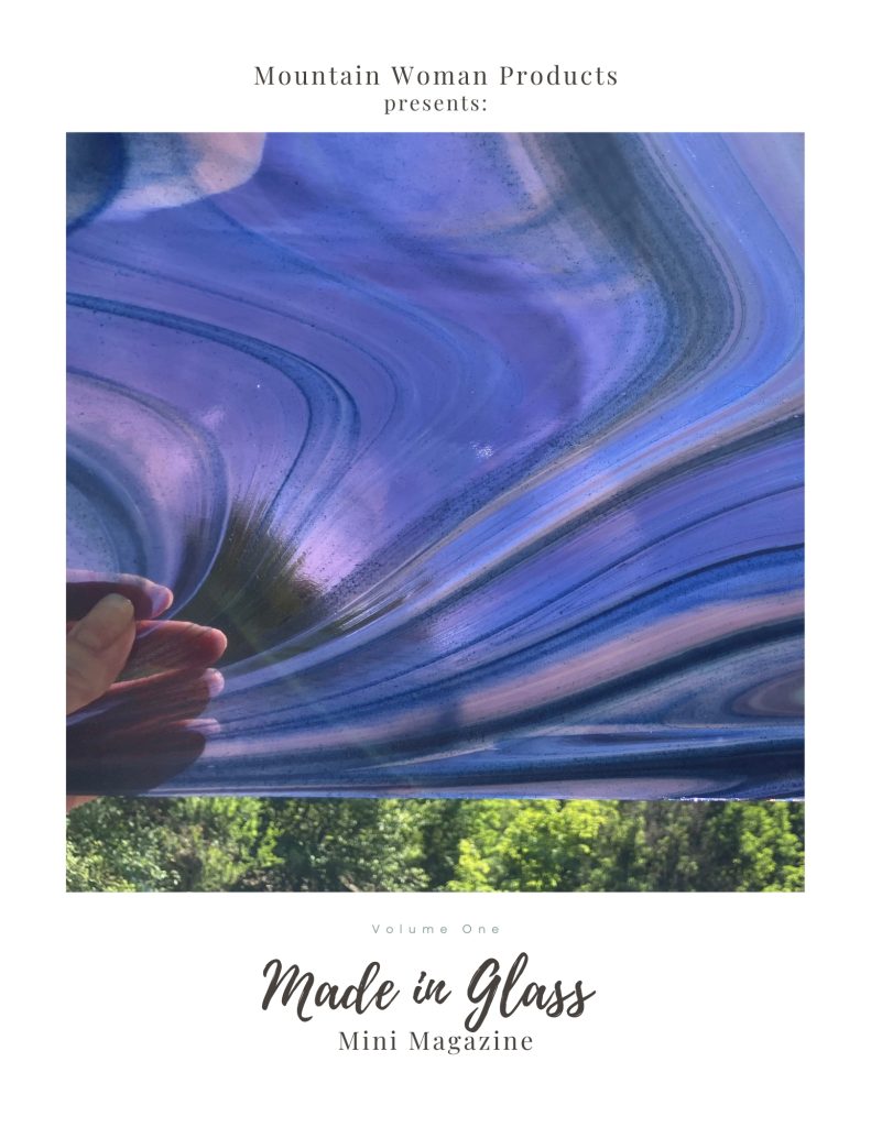Made in Glass Mini Magazine with Oceanside Phantom Galaxy Stained Glass Sheet on cover being held in front of trees by hand presented by Mountain Woman Products