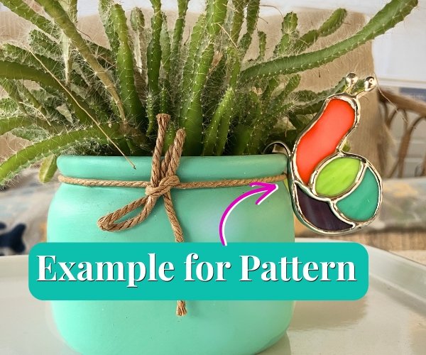 Stained Glass Snail Pot Hugger hanging on an aqua colored pot with green succulent growing in it the snail has an orange body and a lime green aqua and purple shell at the Mountain Woman Products studio