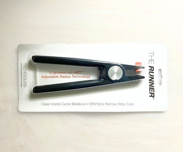 The Runner by Techniglass Running Pliers for stained glass showing black aluminum handles and body and orange adjustable top jaw in white packaging in the Mountain Woman Products studio