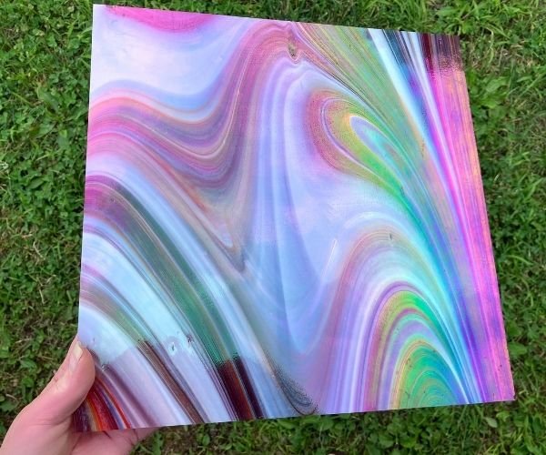 Oceanside Witching Hour Fuser's Reserve Special Edition Stained Glass Sheet held in hand. glass is red and white swirled with rainbowy iridizing all over at the mountain woman products studio