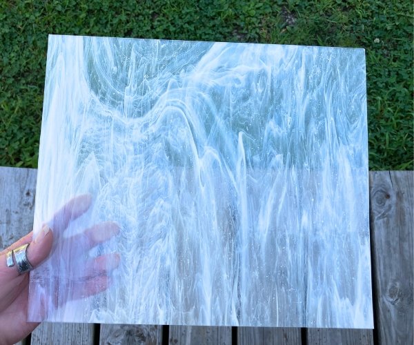 Designer Glass Clear & White Streaky DG1020 stained glass sheet held in hand with grass and wood below at the Mountain Woman Products studio