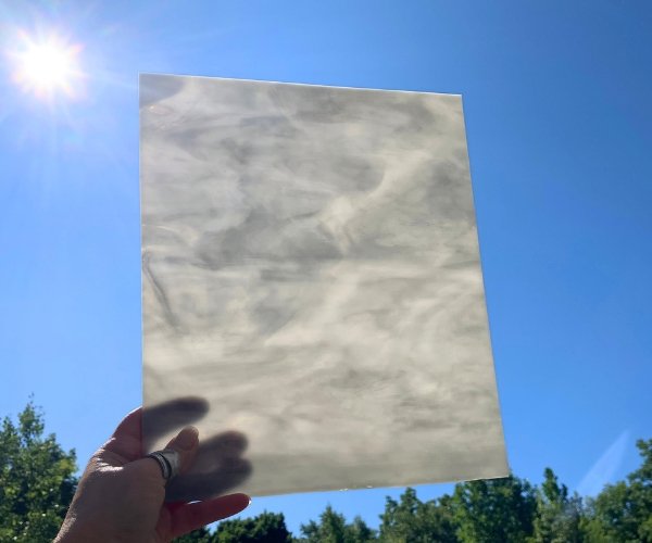 Designer Glass Medium Grey & White Opal held in hand against a bright blue sky showing the white glowing and greys muted at the mountain woman products studio