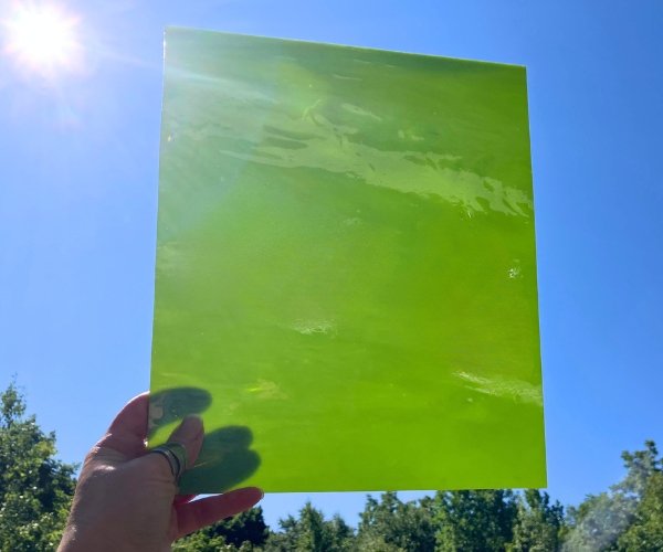 Designer Glass Apple Opal Fusible Stained Glass Sheet with a bright green like if alien barf were attractive held up against a blue sky at the mountain woman products studio