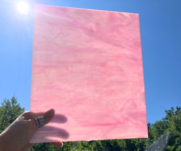 Designer Glass Pink & White Fusible Stained Glass Sheet in a bubble gum pink type color with a hand holding it in front of the sky at the Mountain Woman Products studio