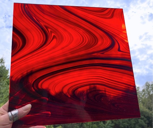 Oceanside Ember Black on Red Fuser's Reserve Limited Edition Stained Glass Sheet showing black swirls on transparent red glass held in front of the sky mountain woman products studio
