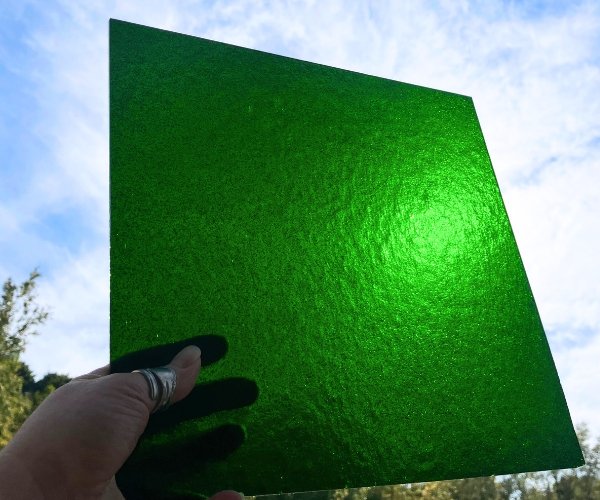 Oceanside Green Aventurine Stained Glass Sheet with a hand holding it up against a blue sky with clouds at the Mountain Woman Products studio
